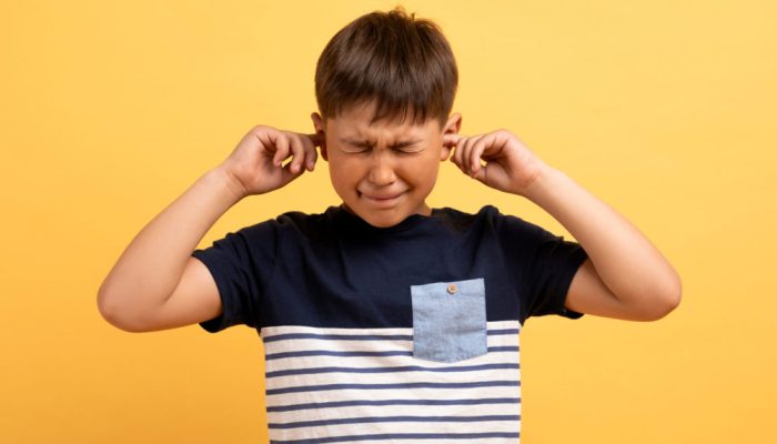 Portrait of angry unhappy irritated preteen boy wearing casual t-shirt covering plugging ears with fingers and squinting isolated on yellow studio background, scared of loud noise voice, bad behaving